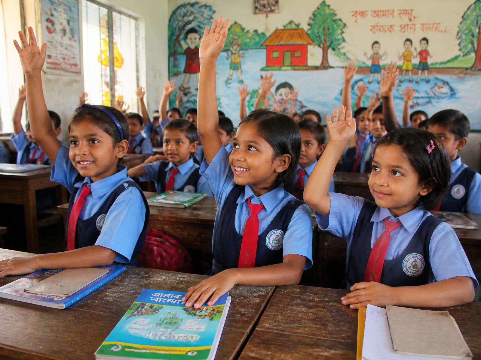 Students raising their hands eagerly during an English Medium class